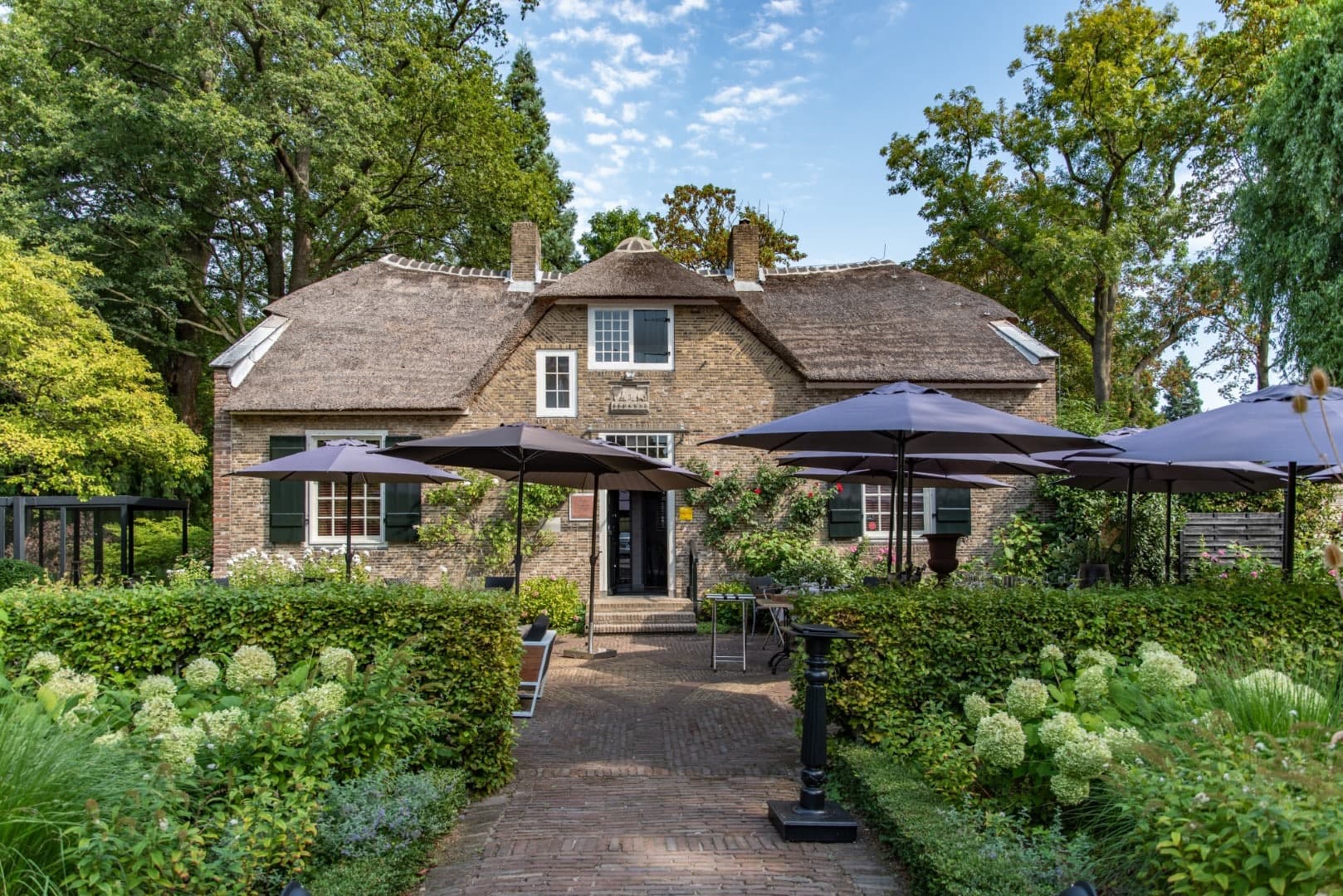 Het historische pand van In Den Rustwat met rieten dak, gezien vanuit de tuin