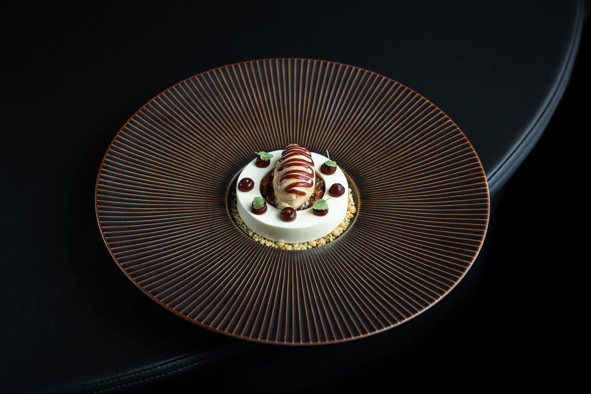 Dessert met een quenelle ijs, rode gelstippen en crumble op een koperkleurig bord